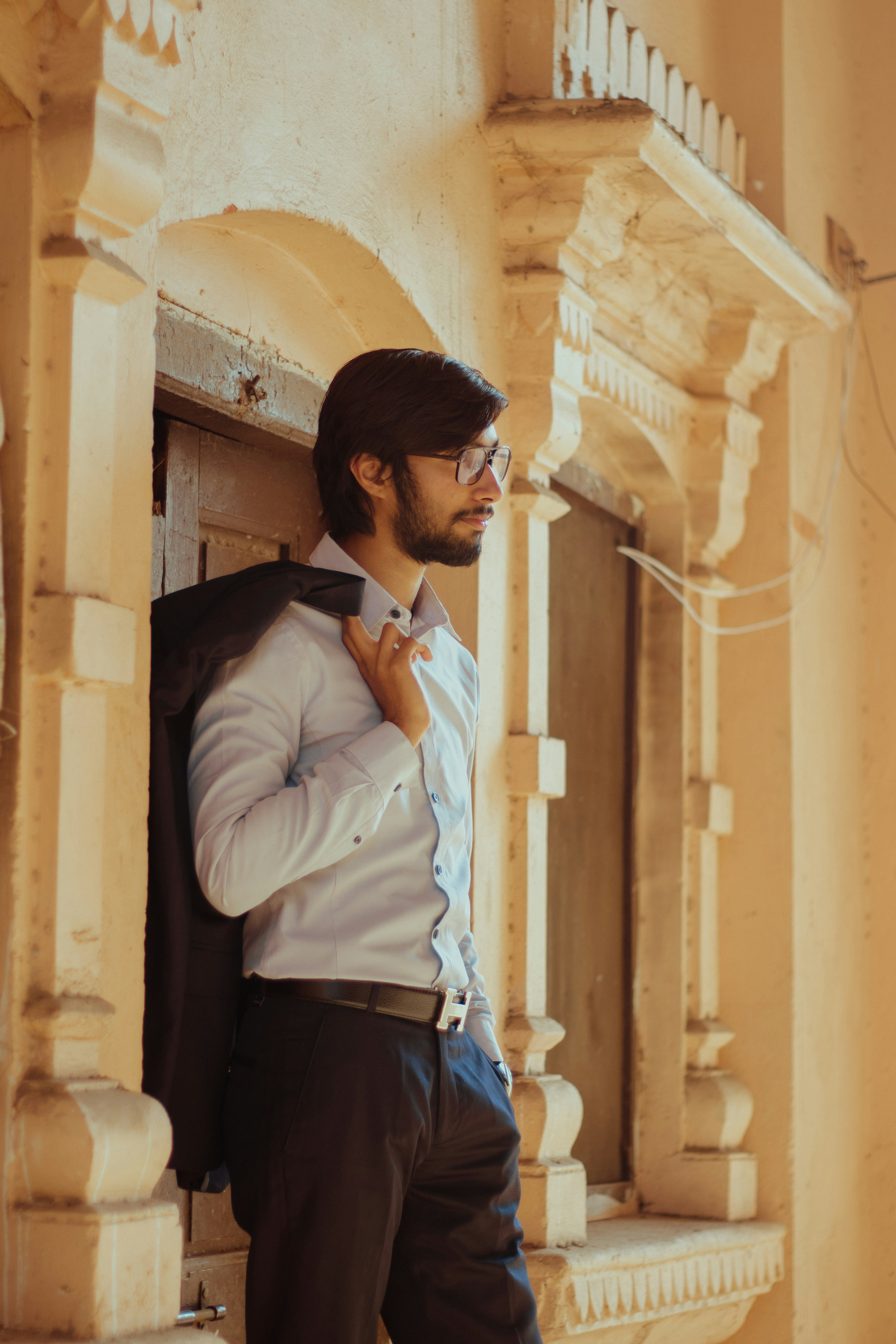 man in white dress shirt and black dress pants standing beside brown concrete building during daytime